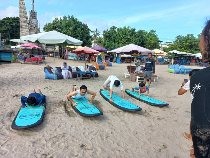 Group Practicing Surfing Skills On Sand With Blue Boards