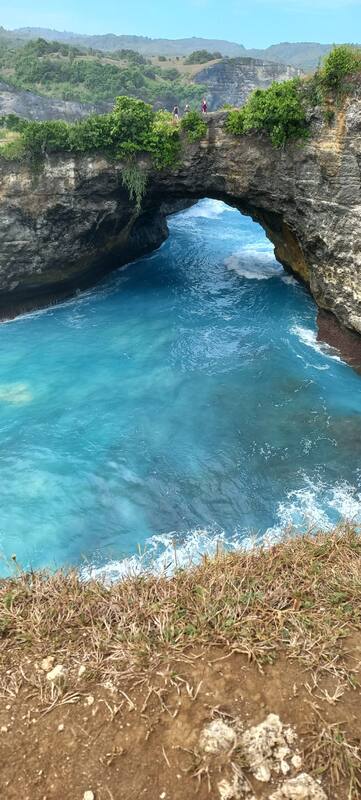 Natural Stone Arch Bridge Over Blue Ocean Water Cliffside View Grass