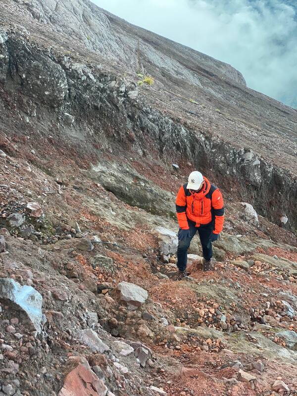 Person In Orange Jacket Climbing Rocky Mountain Slope