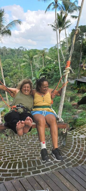Two Women Riding Swing Laughter Tropical Forest Background