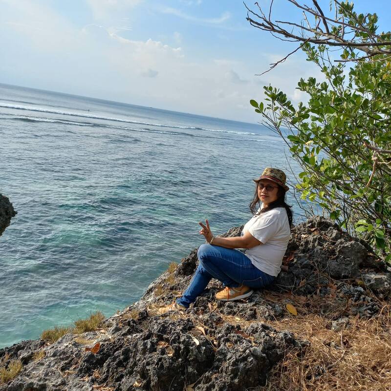 Woman Sitting On Rock Cliff Near Ocean Peace Sign
